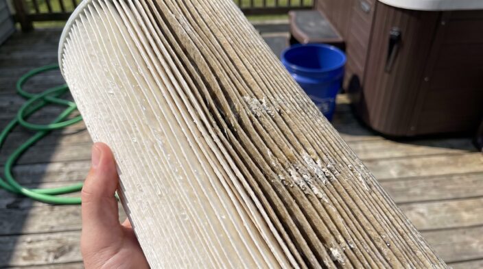 pleated spa filter cartridge showing clean pleats beside oily discolored pleats