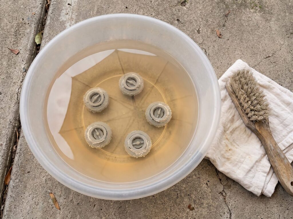 several small jet inserts soaking in a bowl of diluted vinegar solution