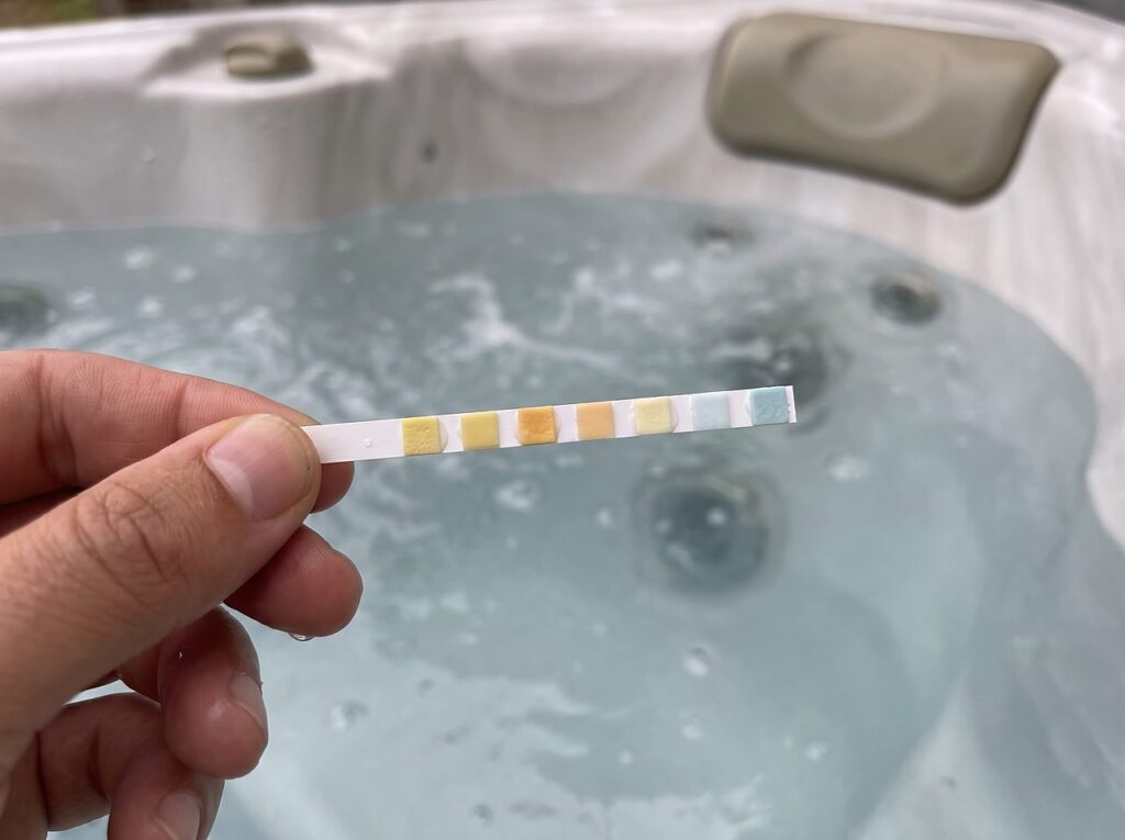 hand holding a water test strip over cloudy hot tub water